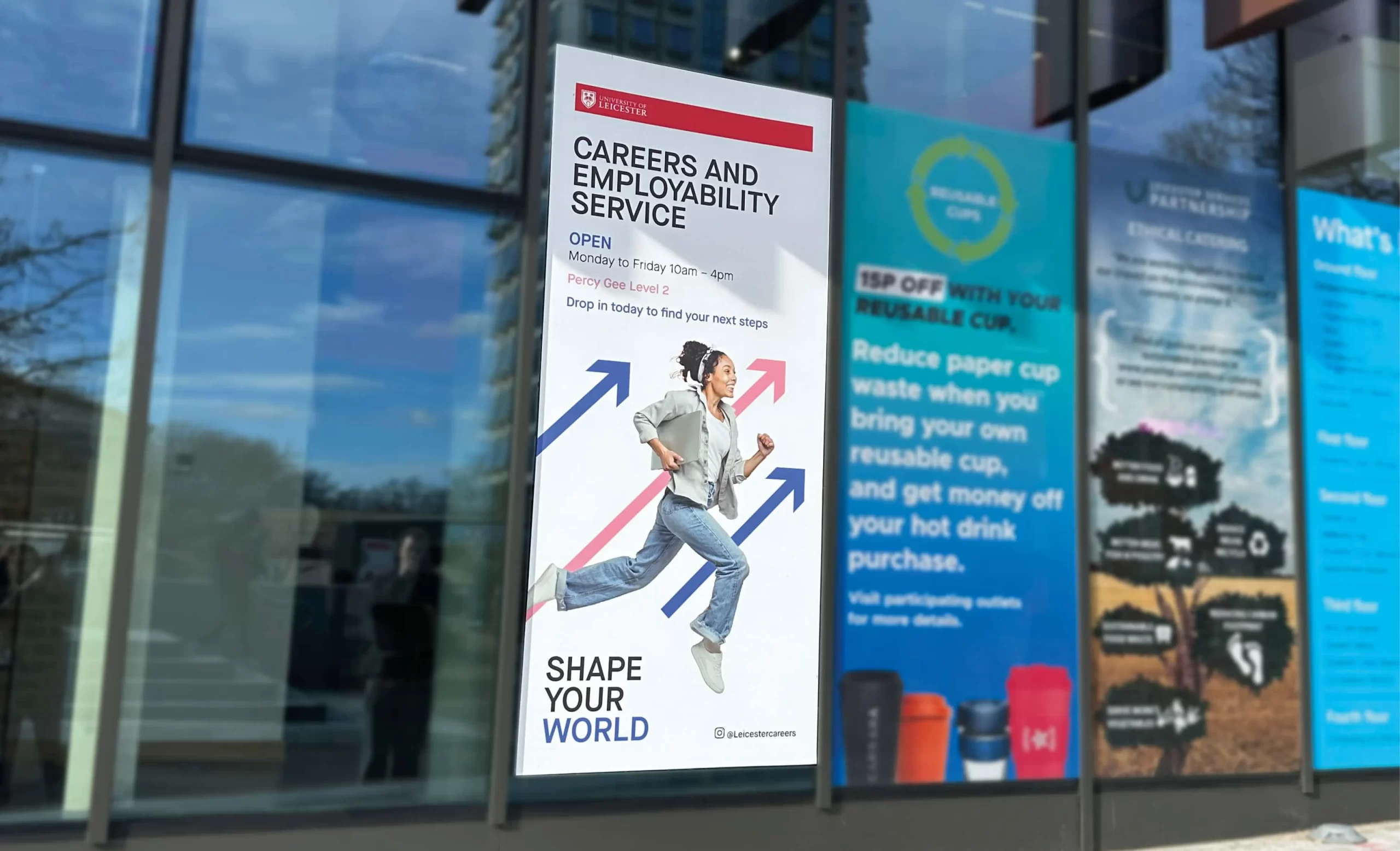 A large poster displayed on the window of a building, promoting the University of Leicester’s “Careers and Employability Service.” The poster features a young woman in motion, with arrows pointing upward in blue and red, symbolising progress and career growth.