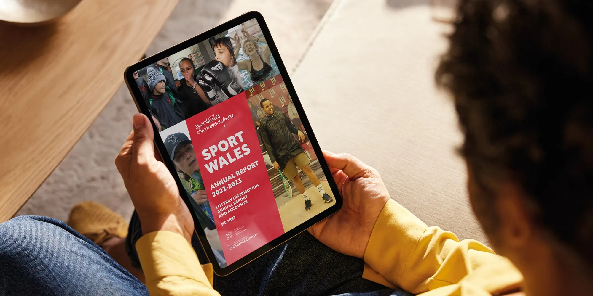 A person holds a tablet displaying the Sport Wales Annual Report for 2022–2023, featuring a bold red banner with white text alongside diverse imagery of athletes and activities.