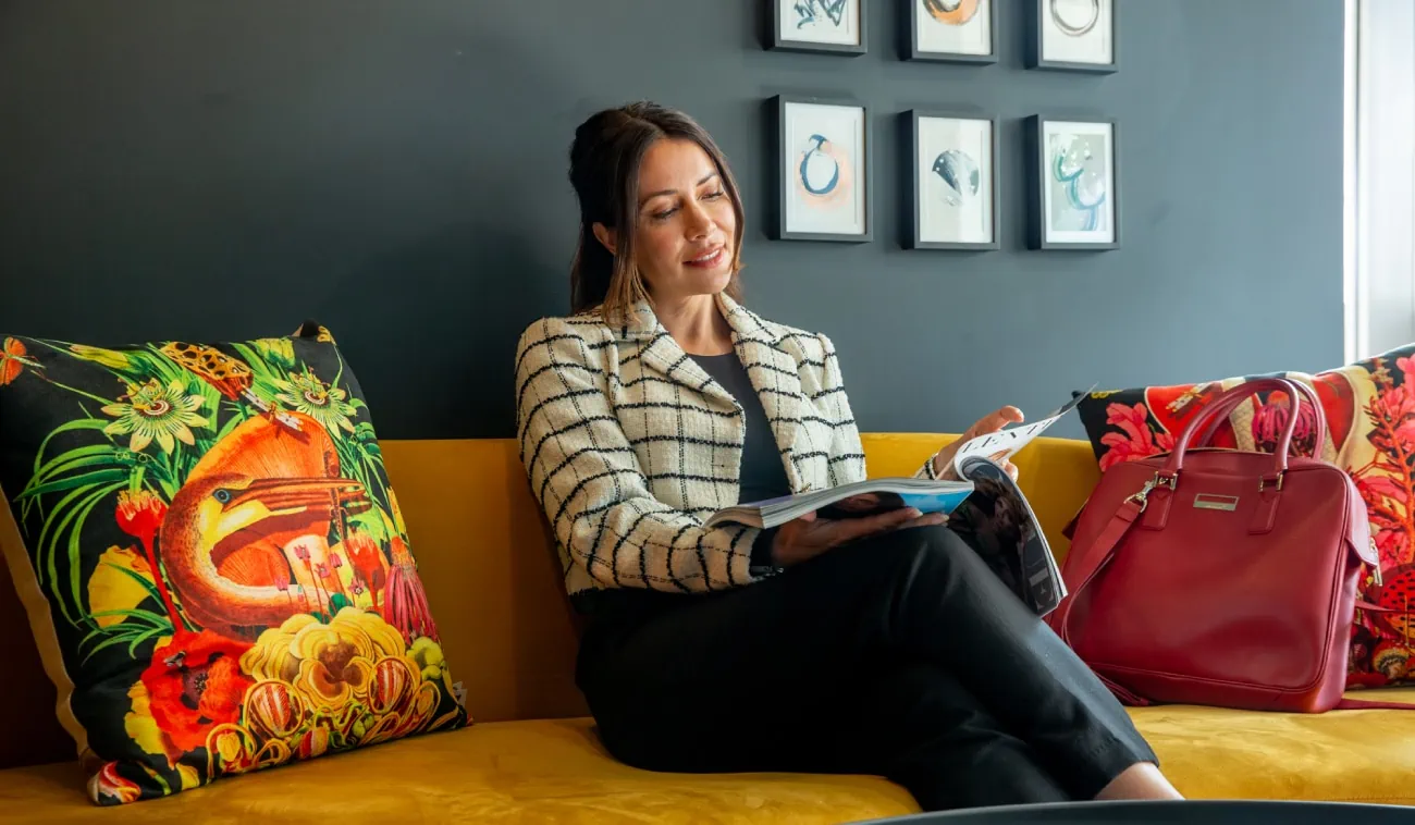 A professional woman relaxes on a vibrant, stylish sofa while reading a magazine.
