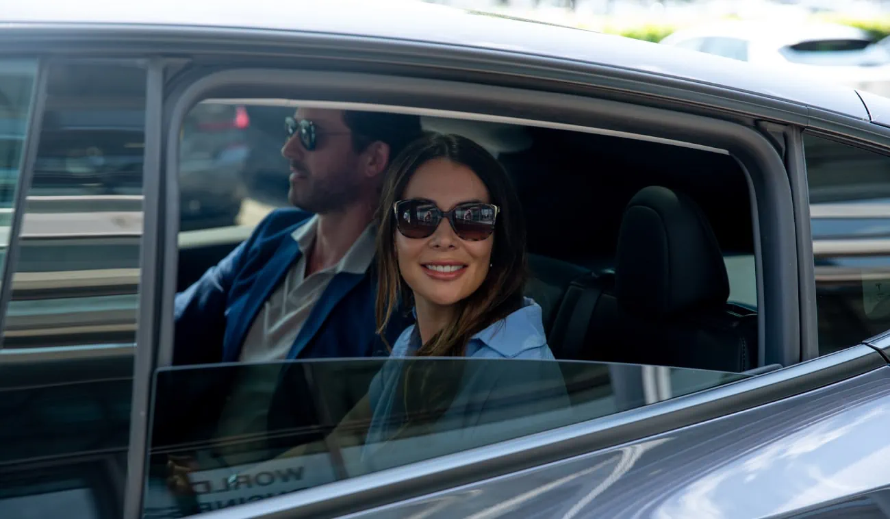 A smiling woman sits in the backseat of a luxury vehicle.
