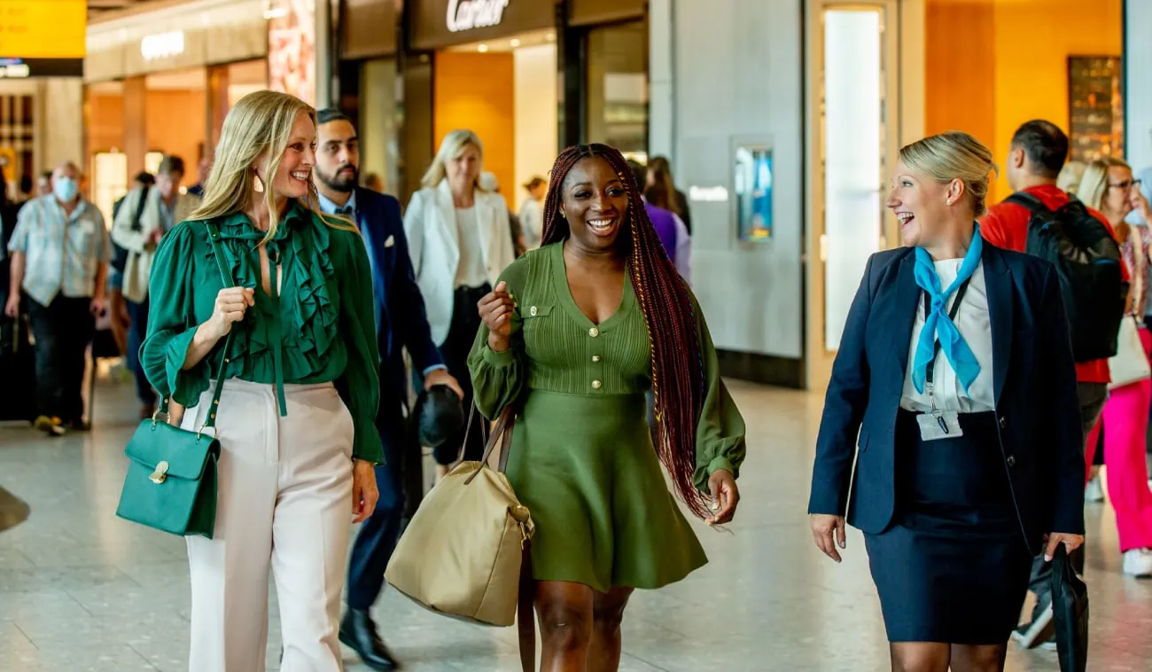 Three women, accompanied by a professional DiamondAir concierge, walk confidently through an airport terminal.