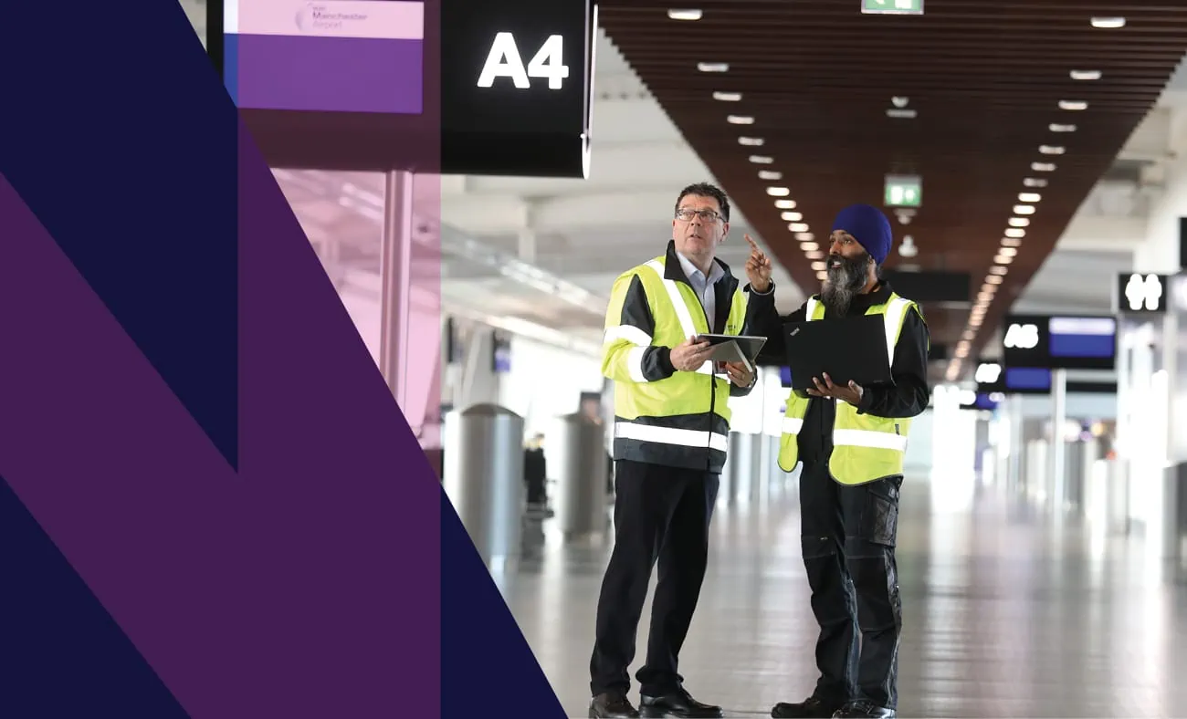 Two Airport workers in high-visibility jackets are pictured collaborating in an airport terminal under the signage of gate A4.