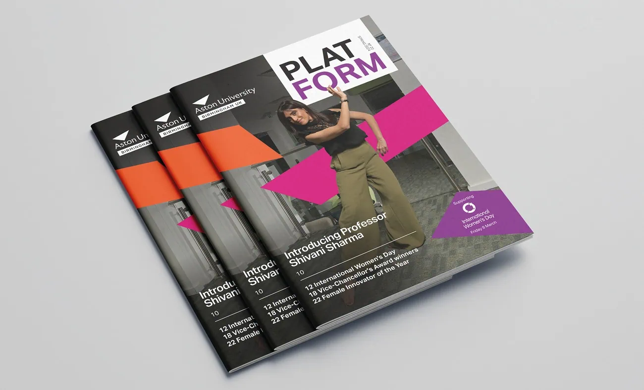A stack of Aston University's "PLATFORM" magazines featuring the cover with a bold geometric design and a dynamic image of a woman posing indoors. The headline reads "Introducing Professor Shivani Sharma," with key articles listed below. The design uses striking pink and orange accents alongside black and purple elements.