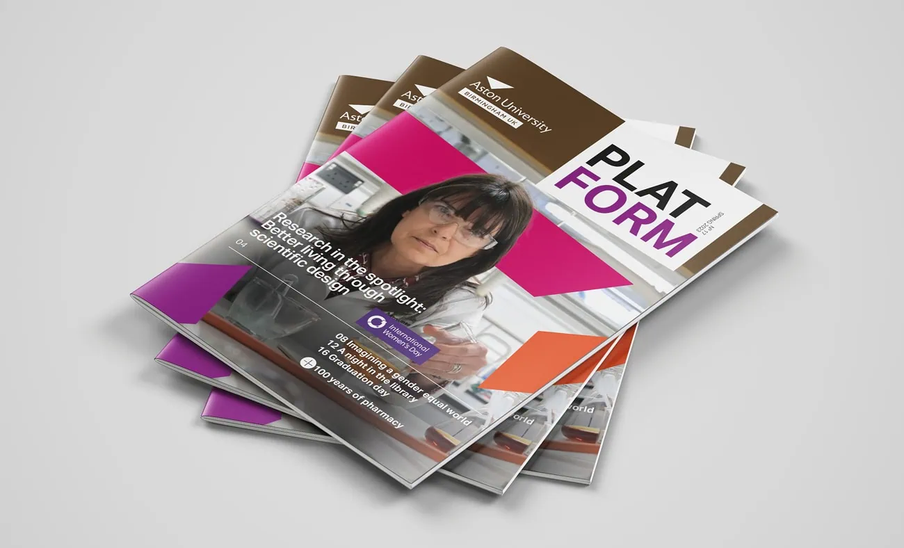 A stack of Aston University's "PLATFORM" magazines featuring a cover image of a researcher in a lab. The headline reads "Research in the spotlight: Better living through scientific design," with geometric accents in pink, orange, and purple. The design includes the Aston University logo at the top and a modern layout that highlights key stories from the issue.