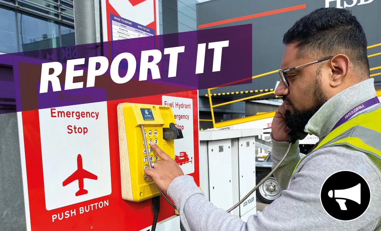A graphic titled "REPORT IT" with a purple banner overlay. The photo shows a Heathrow employee in high-visibility gear using an emergency phone at a designated Aircraft Emergency Stop station. A megaphone icon is displayed in the bottom right corner.
